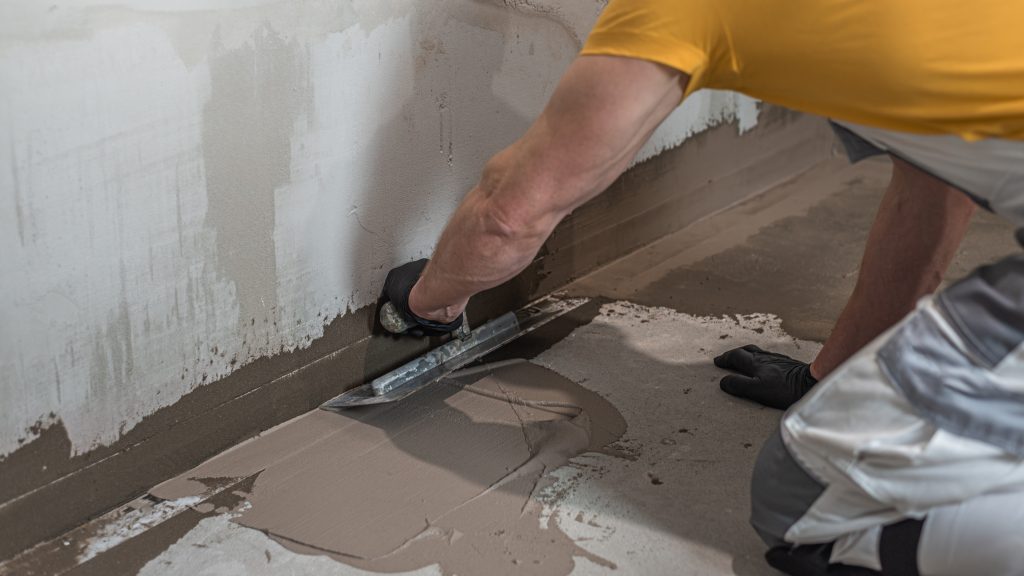 A worker's hand using a trowel for applies a liquid membrane on the bathroom floor. Foolproof waterproofing for a tile bathroom.