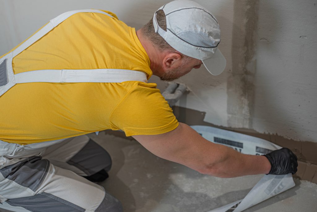 A worker when applying a corner reinforcement tape into liquid membrane. Foolproof waterproofing for a tile bathroom.